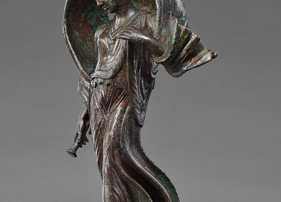 Ancient Roman bronze statuette of Luna, poised on pointed toes with a windblown mantle arched over her head, holding a small object in her right hand.