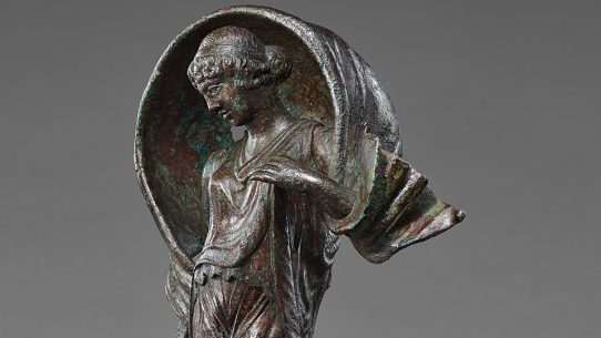 Ancient Roman bronze statuette of Luna, poised on pointed toes with a windblown mantle arched over her head, holding a small object in her right hand.