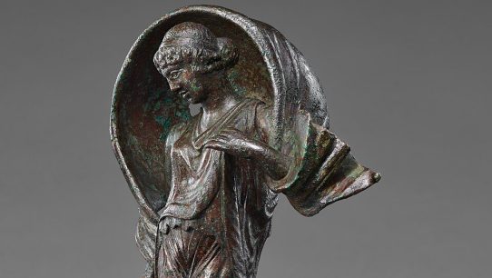 Ancient Roman bronze statuette of Luna, poised on pointed toes with a windblown mantle arched over her head, holding a small object in her right hand.